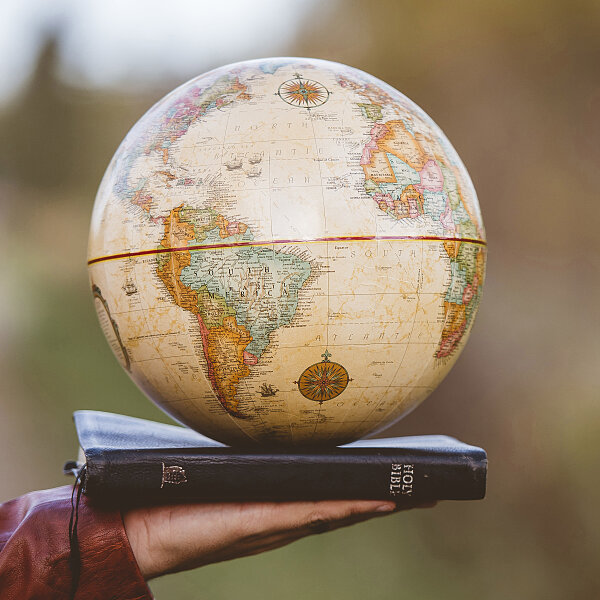 closeup shot person holding bible with desk globe top